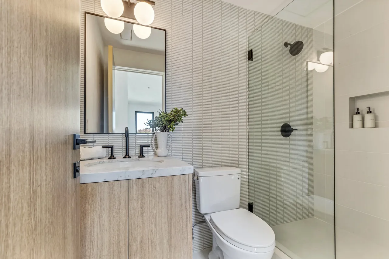 This bathroom features a floating vanity with a marble countertop, black matte faucets, and a glass shower enclosure with wall niches.