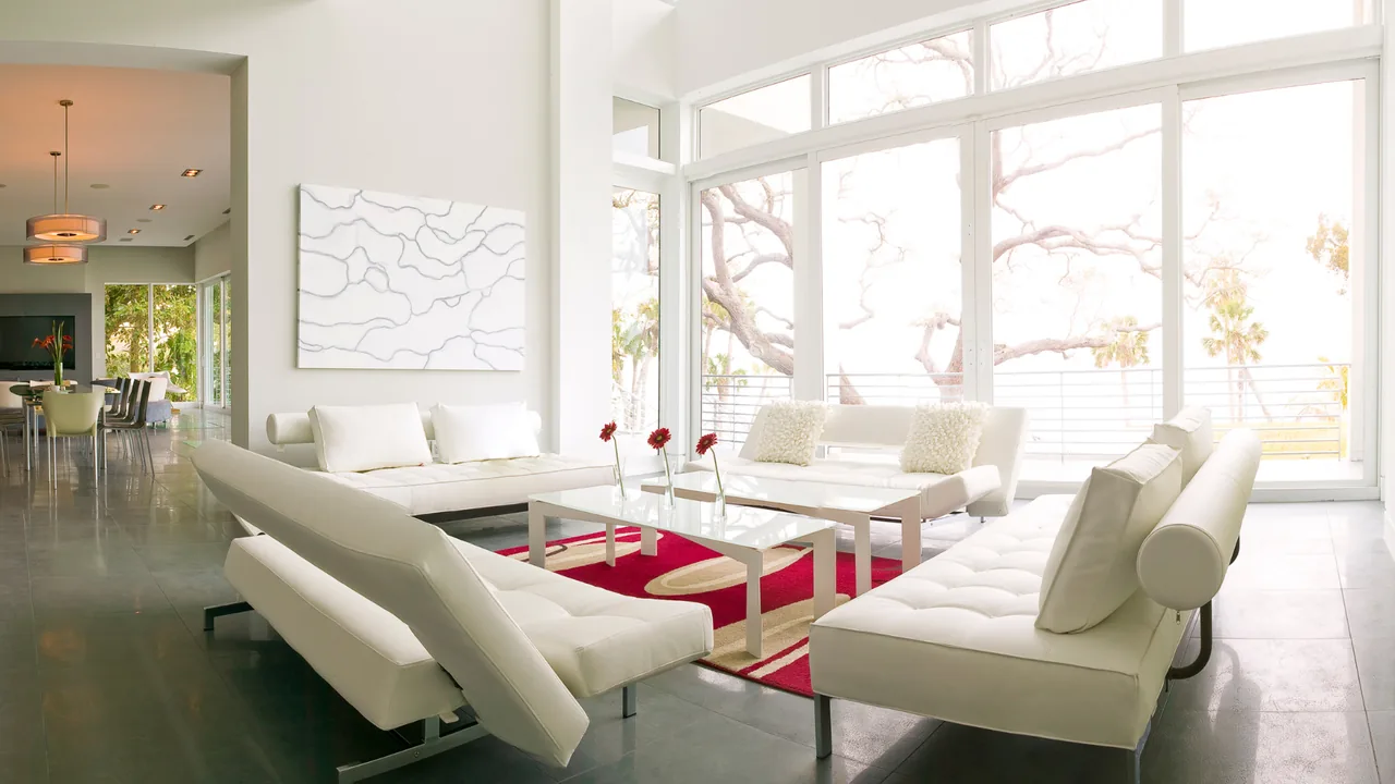 Living room with white contemporary sofas, a glass coffee table, and expansive floor-to-ceiling windows bringing in natural light.