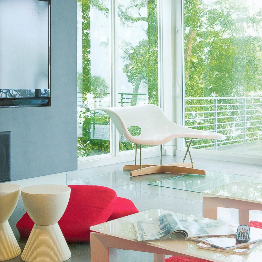 Living room features floor-to-ceiling windows with horizontal railing visible outside and modern white chair with wood base.