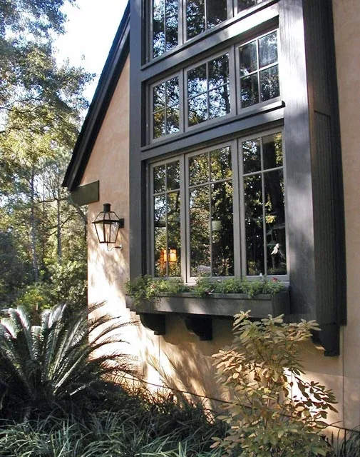 Steep gable roof with large divided lite black window frames and a planter box on a stucco facade with shrub landscaping.