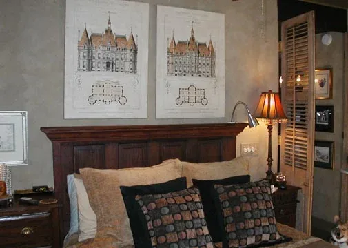 Bedroom featuring a dark wood headboard, decorative framed architectural prints, and a table lamp with a traditional shade.