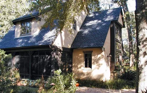 The Verneuille Residence features a steep gable roof and a screened-in porch area under heavy tree shade.