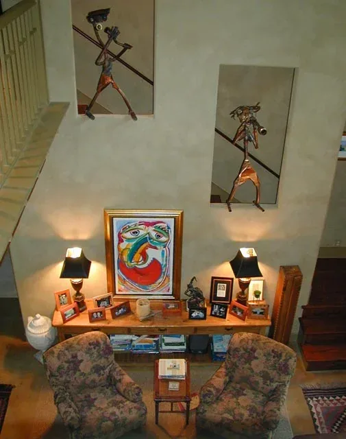 Living area with floral armchairs, artwork, and lantern wall sconces illuminating a textured wall in the Verneuille Residence.
