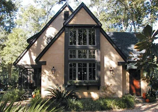 The Verneuille Residence features a steep gable roof and black window frames on a beige stucco exterior.