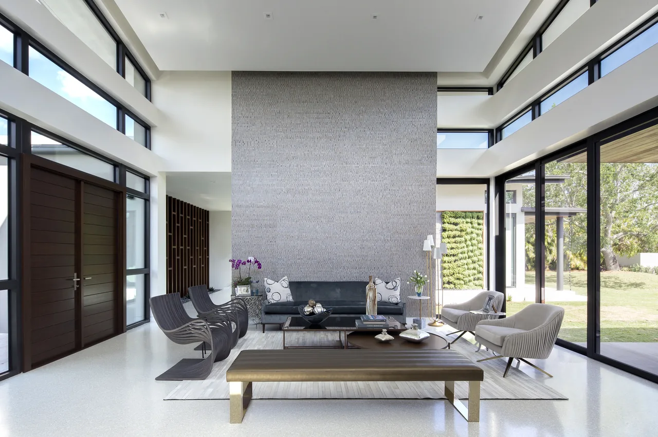 Living room features large windows, a tall textured wall, and modern seating with a bench and accent chairs.