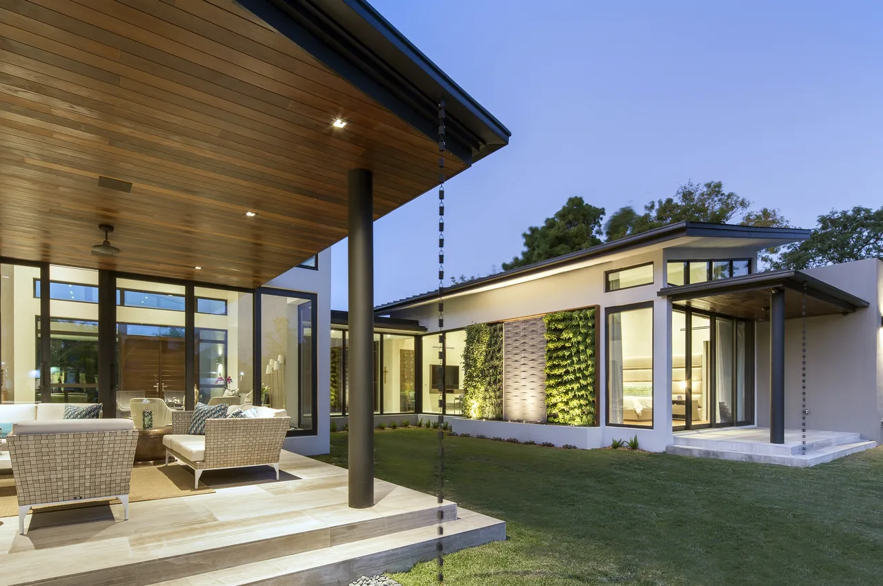 The ALF Residence showcases a large cantilevered roof covering an outdoor living space with wicker seating and a vertical garden on the house facade.