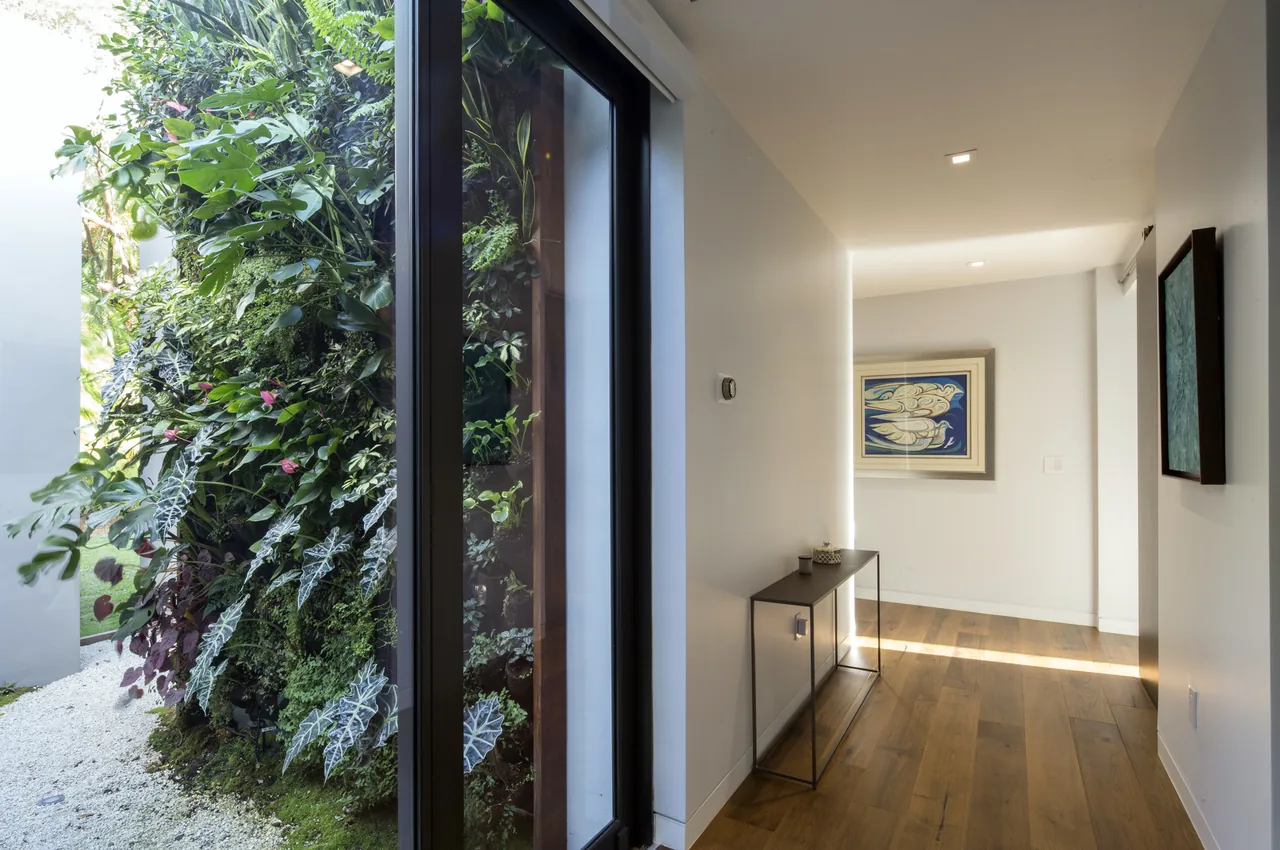 Hallway in ALF Residence by SDH Studio Architecture + Design, featuring vertical garden wall visible through glass door.