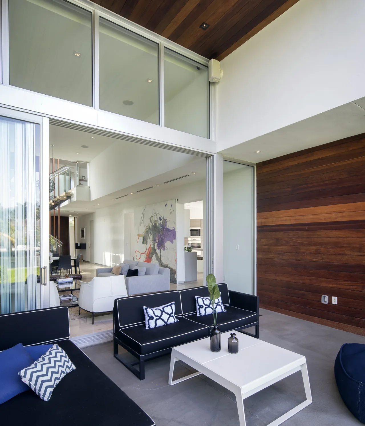The Wex Residence features an outdoor patio with black cushioned seating and a white coffee table that opens into a bright living space through sliding glass doors.
