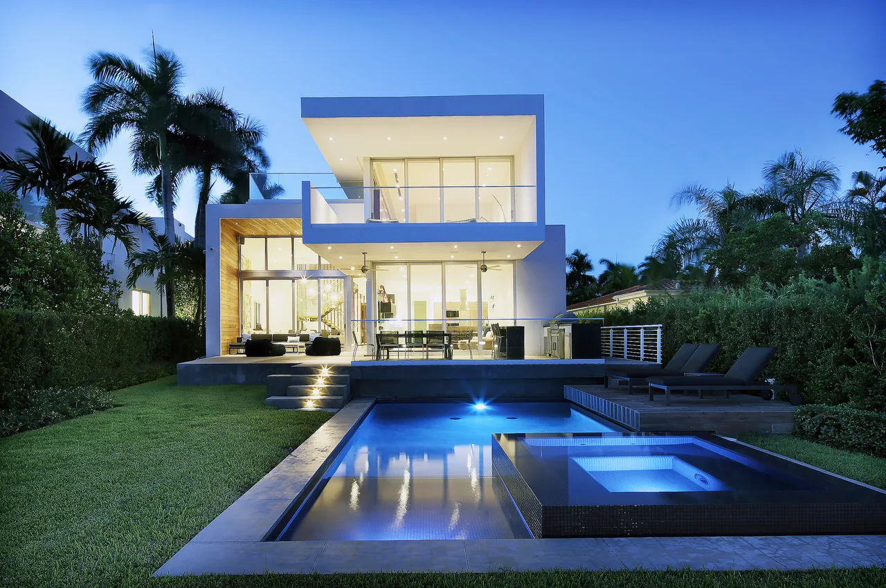 The Wex Residence features a cantilevered upper floor, large sliding glass doors, and an illuminated pool with seating deck.