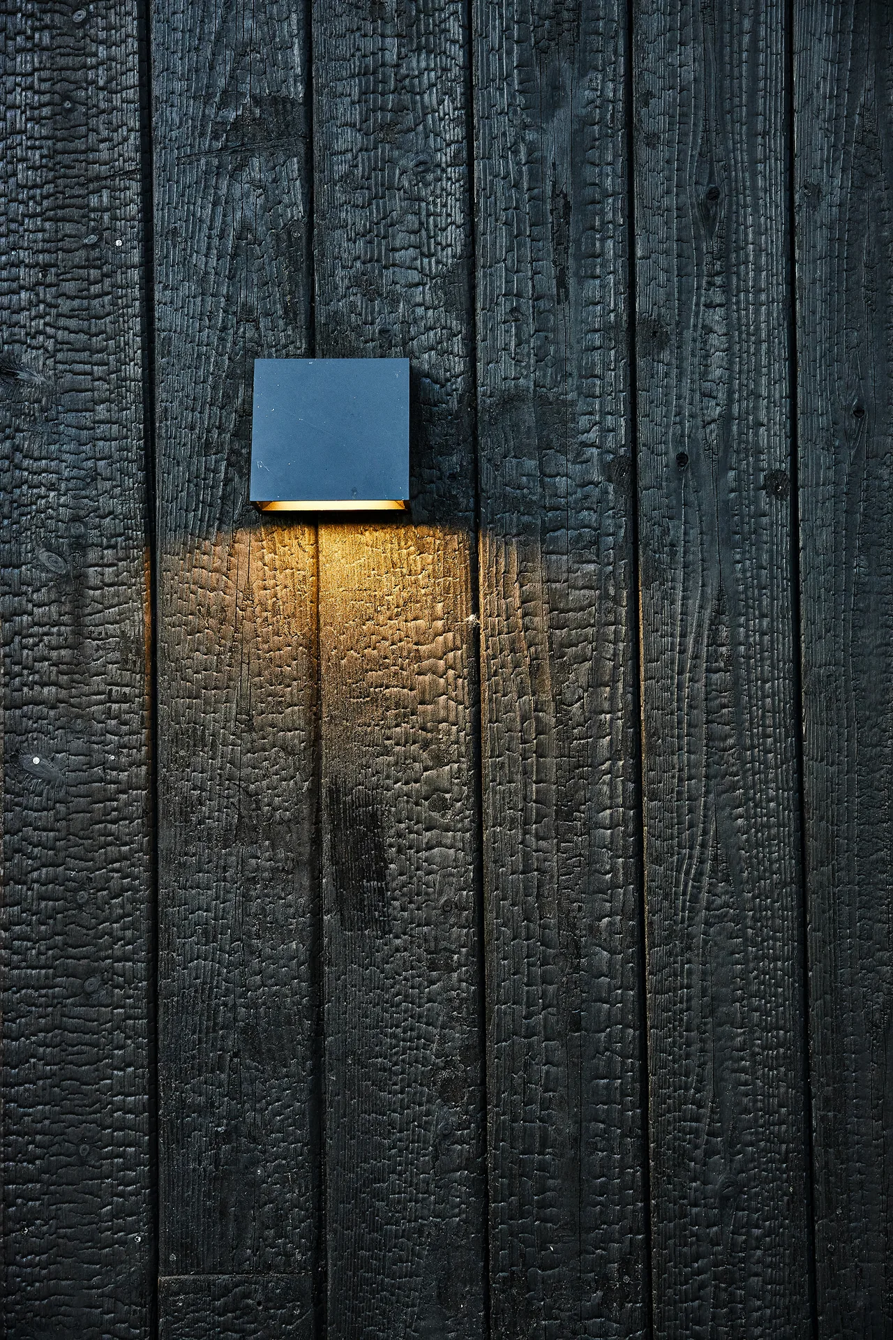 A metal wall sconce illuminates the charred wood siding of the A-Frame Treehouse exterior.