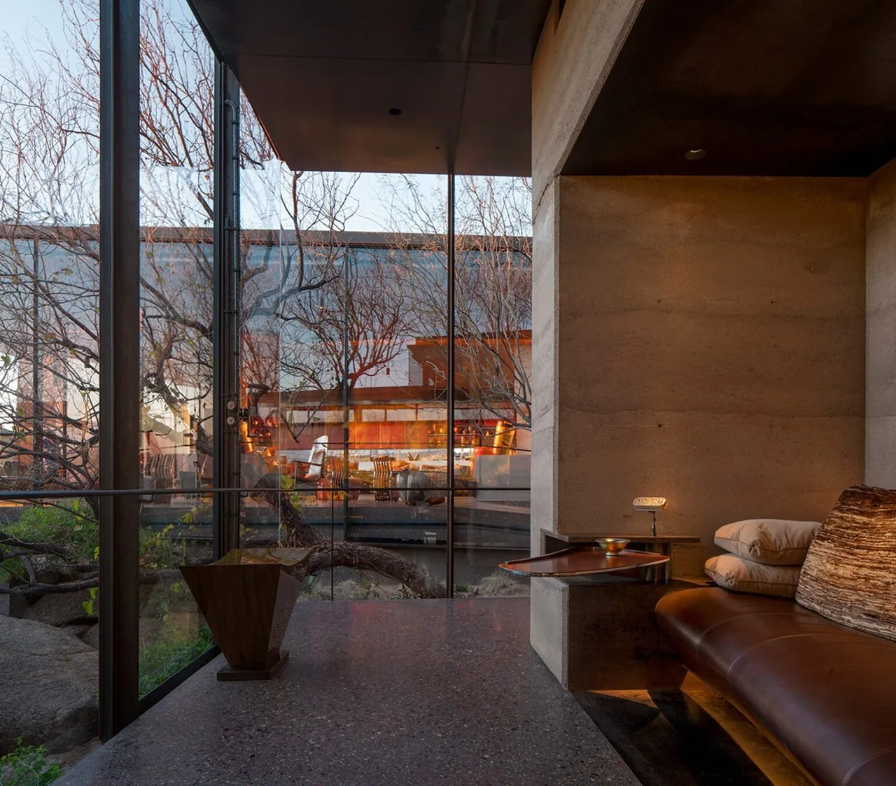 Desert Courtyard House interior with rammed earth walls, floor-to-ceiling glazing, and an integrated leather bench seating area.