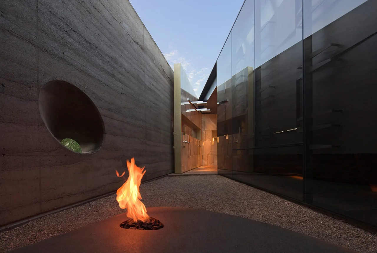 The Desert Courtyard House features a minimalist courtyard with rammed earth walls, gravel ground, and an integrated outdoor fire pit.