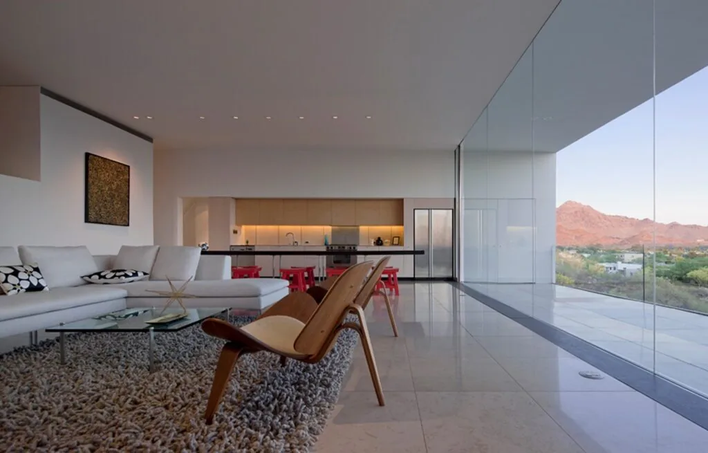 Dialogue House living room features floor-to-ceiling glazing and clean lines with a grey shag rug and white sectional sofa.