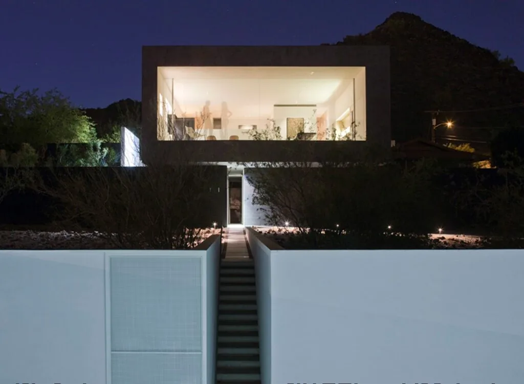 Dialogue House features a cube-like illuminated upper level with floor-to-ceiling glazing above a dark lower level accessed by a narrow stairway.