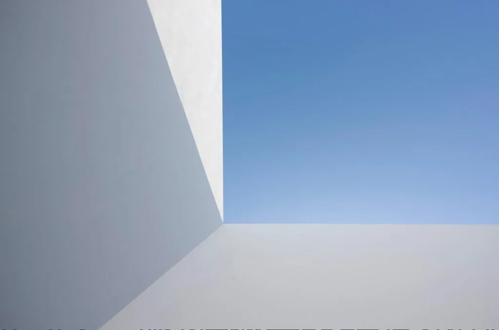 Minimalist white stucco exterior walls meet sharply below a clear blue sky at Dialogue House.