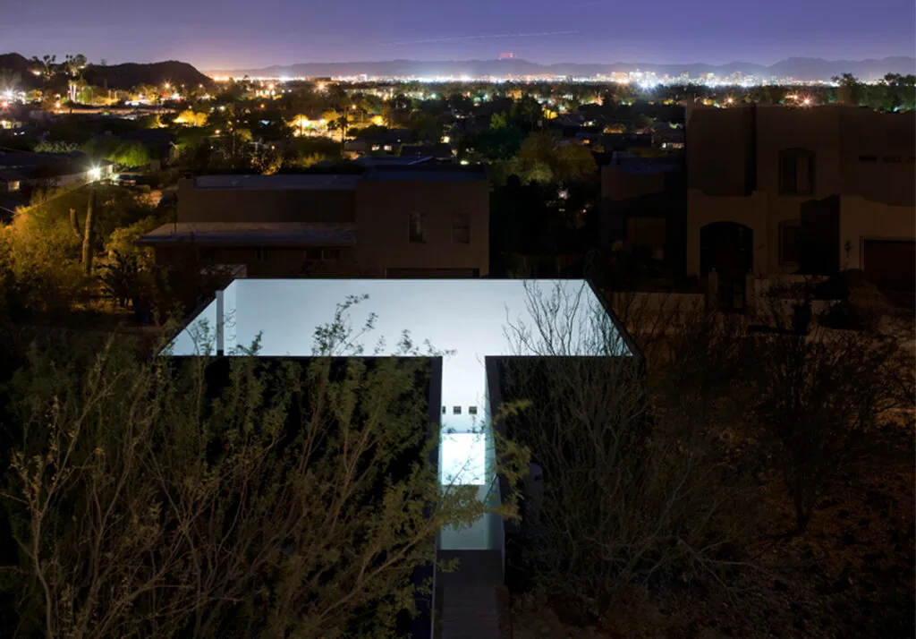 The Dialogue House features a brightly illuminated narrow courtyard enclosed by white stucco walls at night.