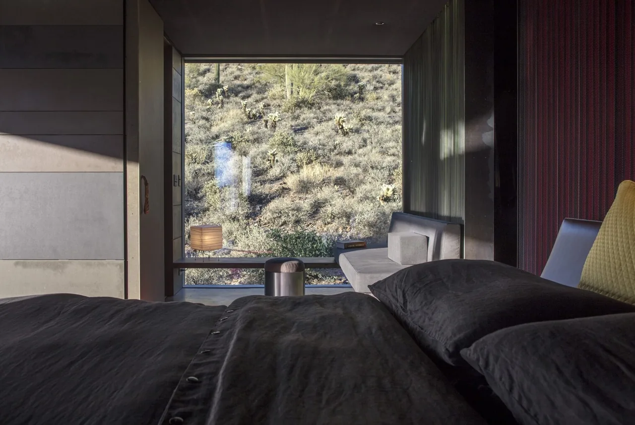 Bedroom interior with black bedding and a large window overlooking desert landscape at Hidden Valley Desert House.