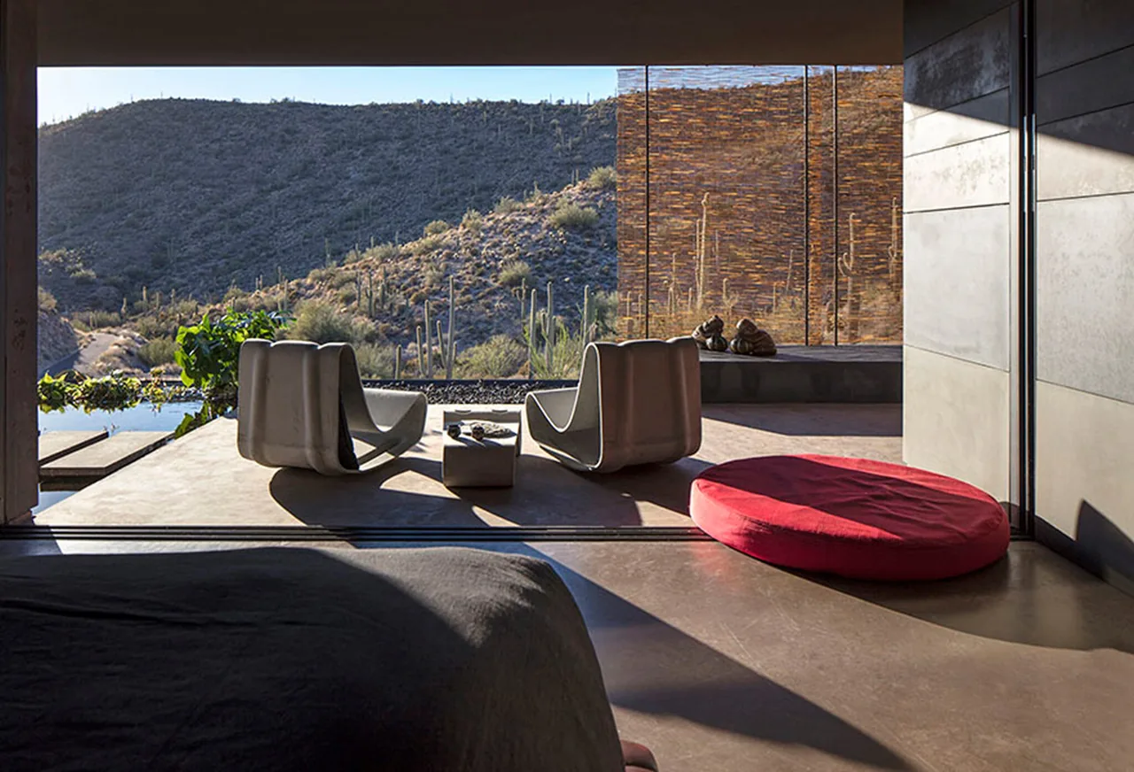 Bedroom opens to a patio with modern chairs overlooking a desert hillside at Hidden Valley Desert House.