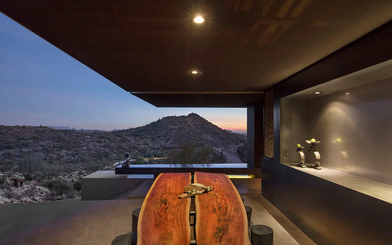 Covered outdoor patio with a natural wood slab dining table overlooking desert hills at sunset.