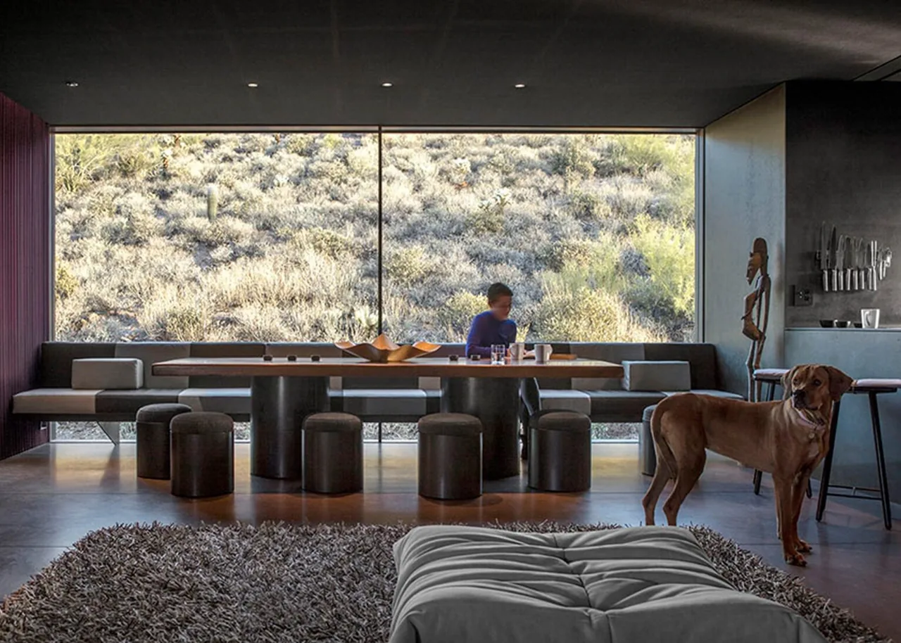Dining area with built-in bench seating and large window overlooking desert landscape in Hidden Valley Desert House.