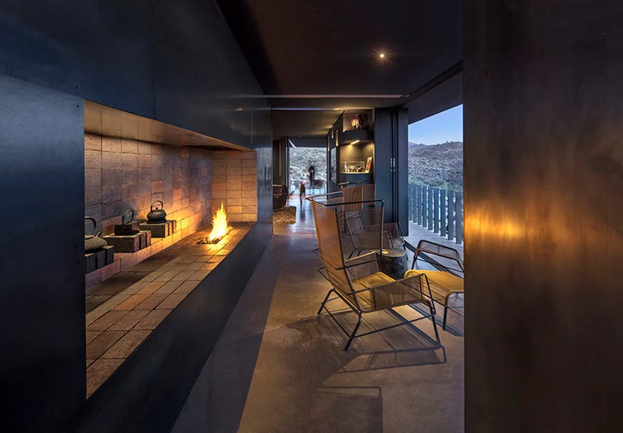 The Hidden Valley Desert House features a sleek fireplace and seating area opening to the desert landscape.