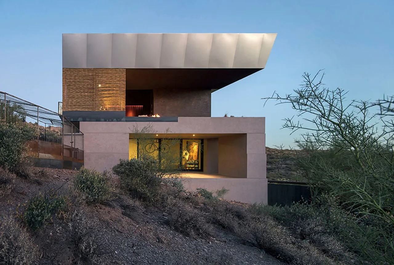 Hidden Valley Desert House features a cantilevered flat roof and stacked wall design on a sloping desert site.
