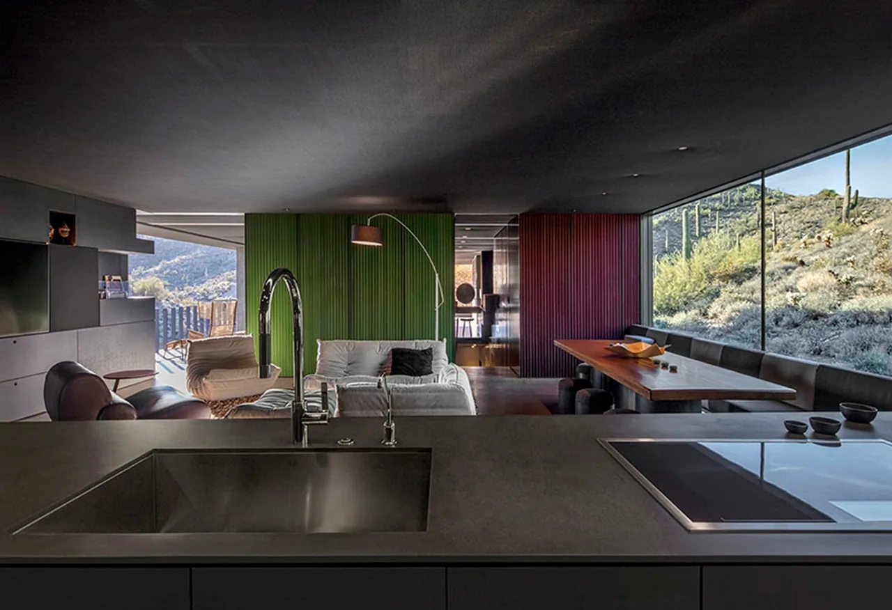 Interior view from kitchen island towards living and dining spaces with stacked wall panels and desert landscape outside.