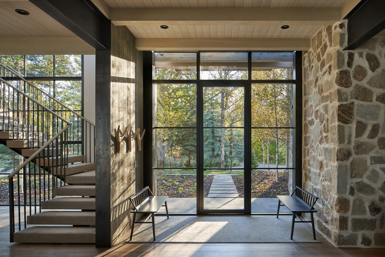 Entryway features large grid windows, stone wall, and a visible modern staircase at Whitefish Lakehouse.
