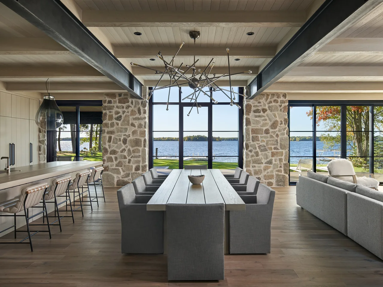 Dining area in Whitefish Lakehouse with lake view through large grid windows and stone pillars framing the space.