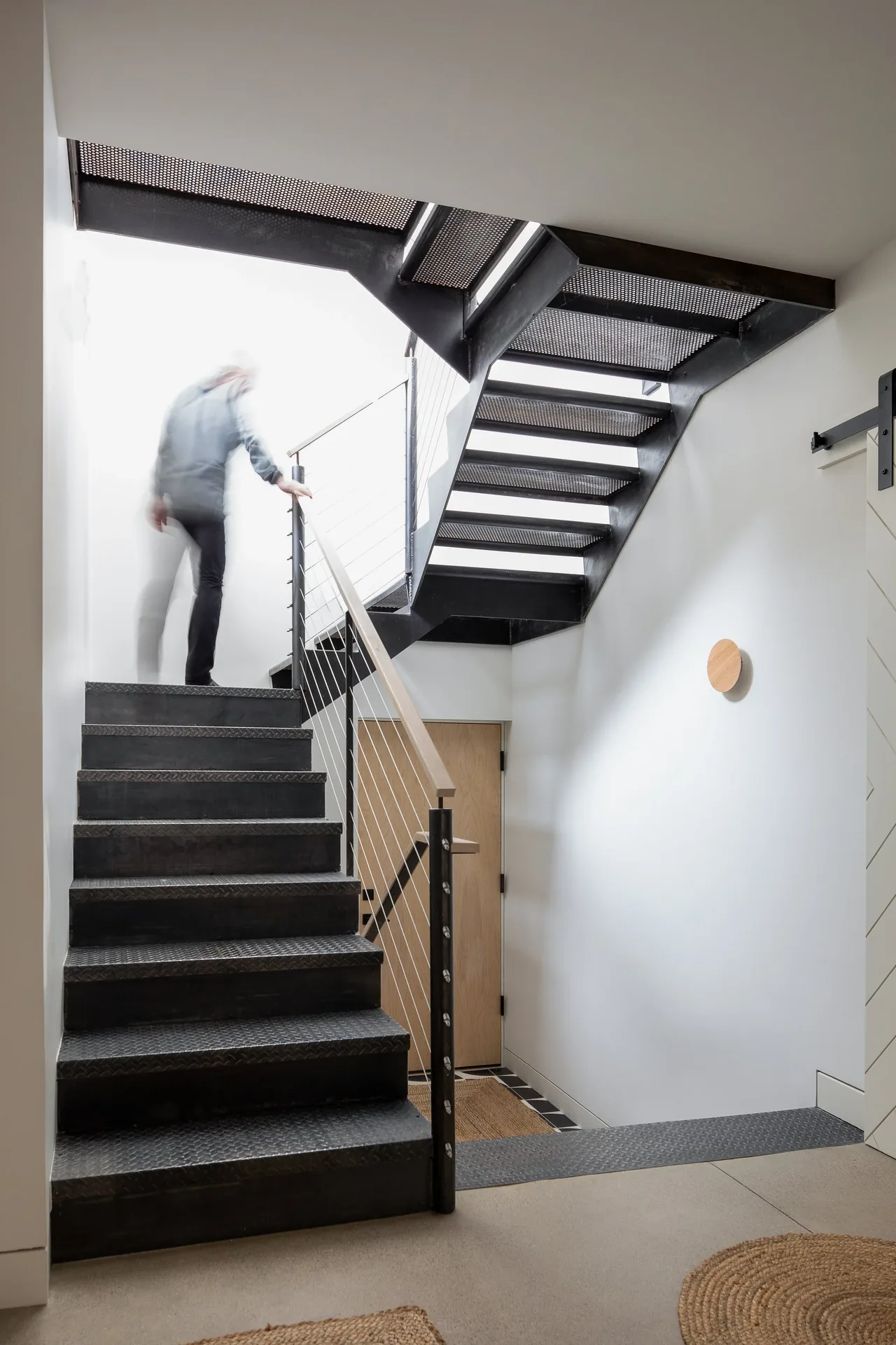 Modern metal staircase with perforated steps and cable railing in a bright entry space.