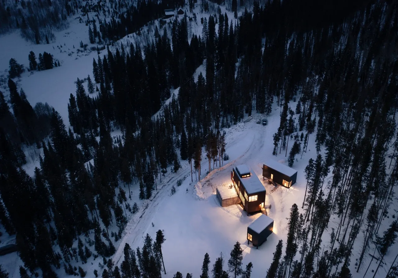 The GCR-8 project by DAVIS URBAN features illuminated modern structures with metal siding in a snowy forest.