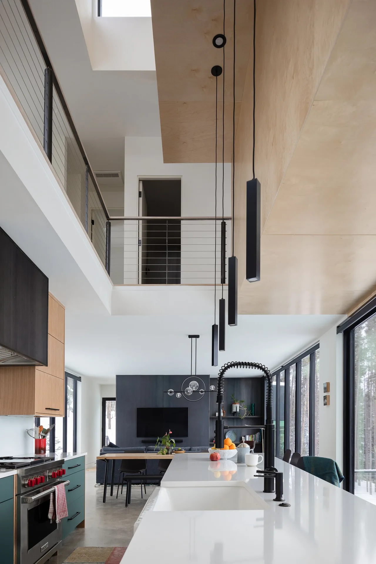 Modern kitchen and dining area with large windows and a two-story ceiling featuring multiple black hanging pendant lights.