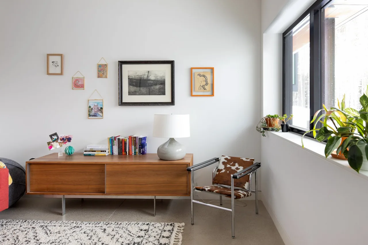 Modern living area corner with wood sideboard, animal print chair, decorative art, and plants on a window ledge.