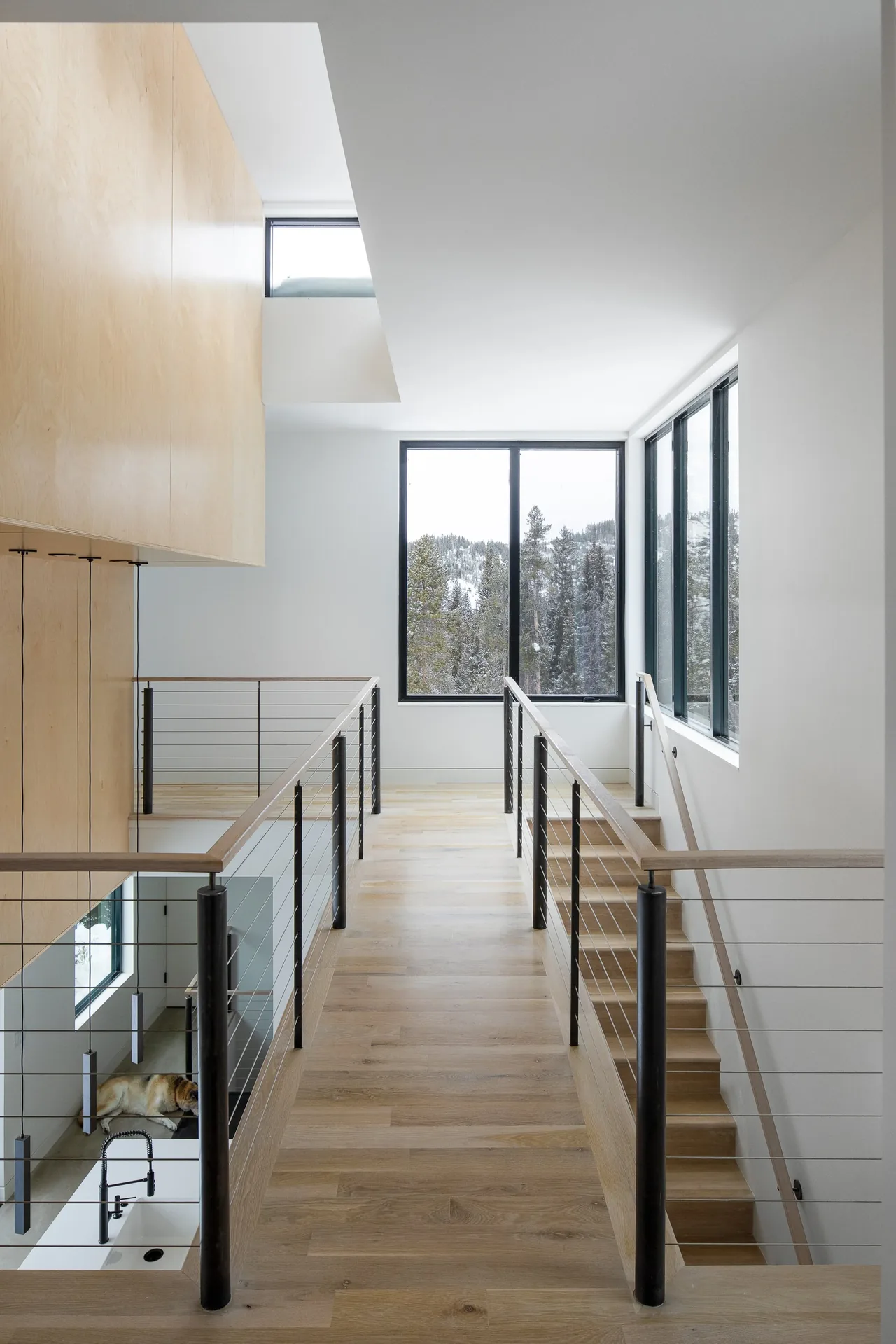 Two-story interior catwalk with cable railing overlooks kitchen area with black faucet and concrete floor below.