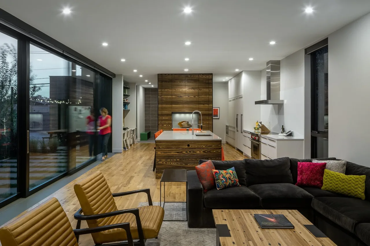Open living room and kitchen featuring wood flooring, a large island, and floor-to-ceiling glazing along one wall.
