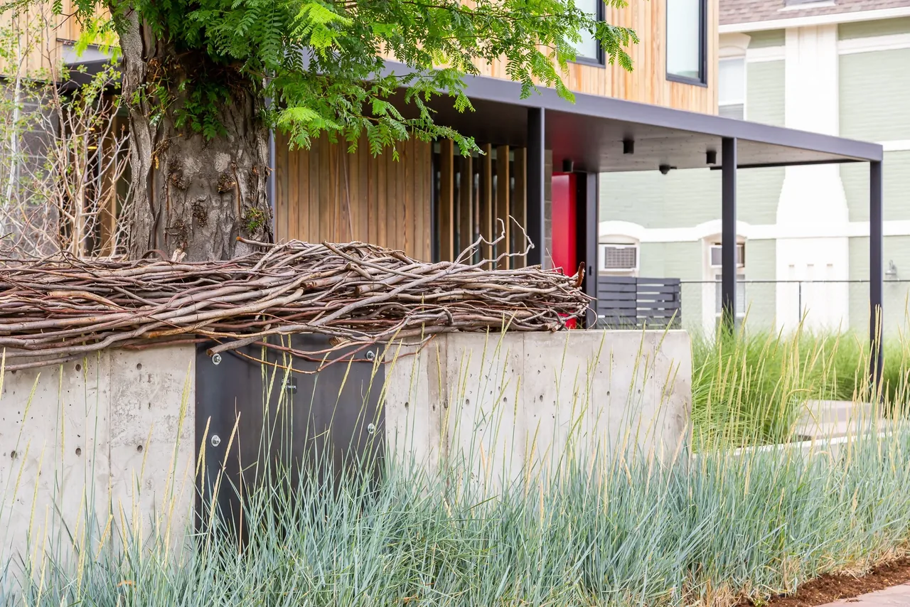 Modern residence exterior with vertical wood siding, black metal pergola, and integrated concrete bench in a grassy yard.