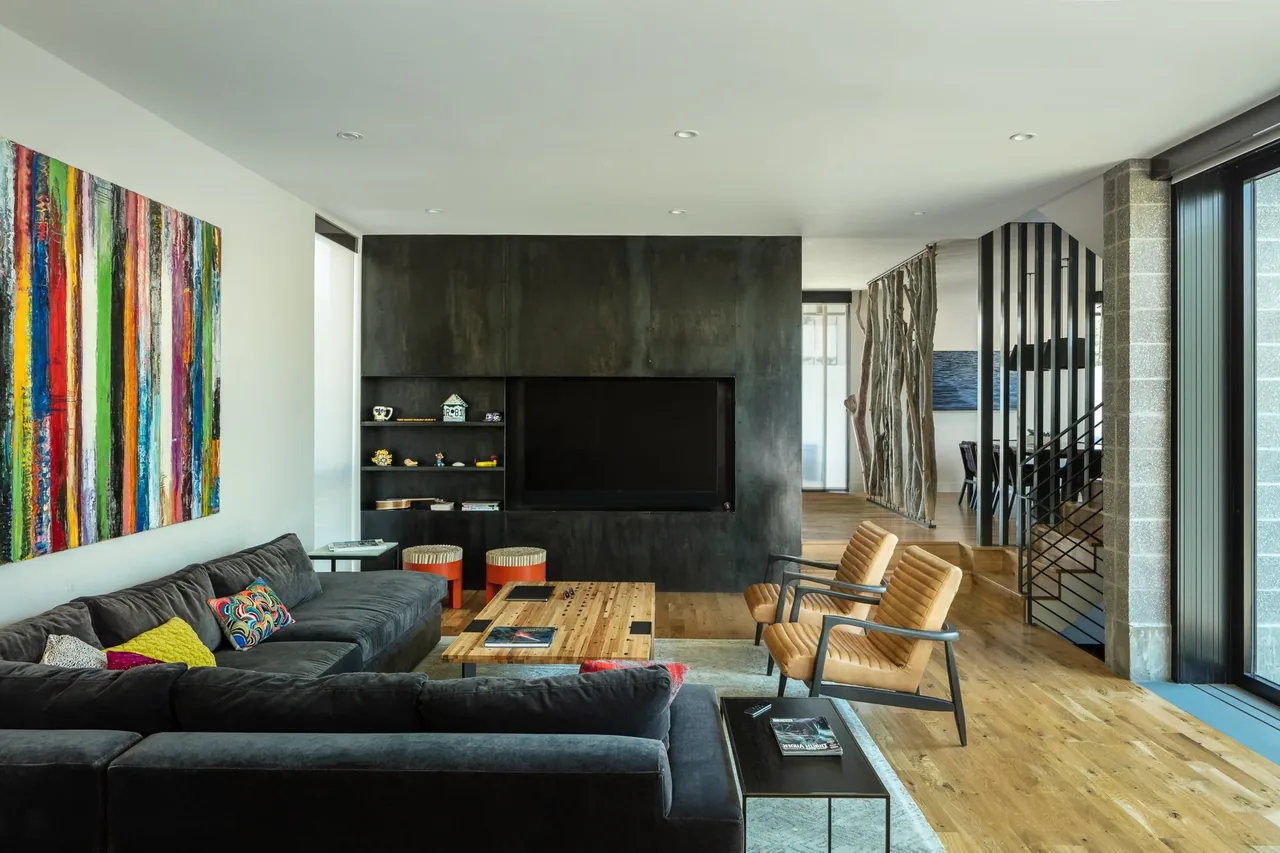 Living room at RiNo residence features a black sectional sofa, colorful pillows, and a black metal wall with built-in TV and shelves.