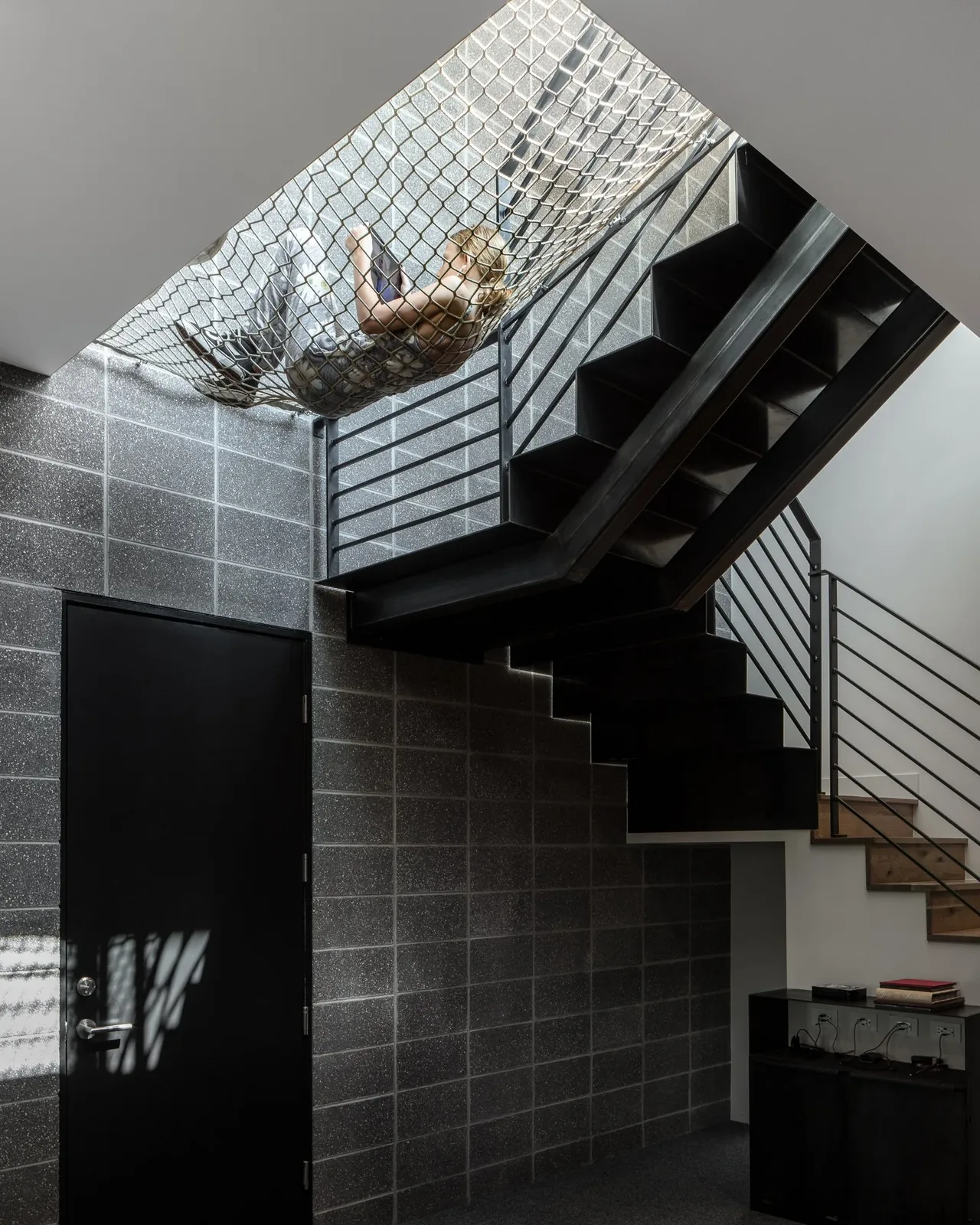 Interior stair area with industrial gray block wall and a suspended net hammock under black metal stairs.