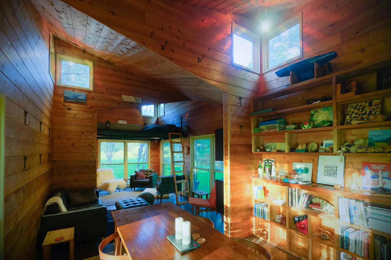 Wood-paneled playhouse interior featuring a loft bed accessed by a ladder, built-in wooden shelving, and large windows providing natural light.