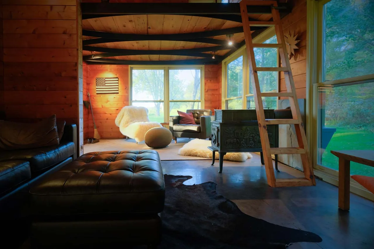 Cozy interior of a small playhouse featuring wood-paneled walls, large windows, and a cast iron stove.