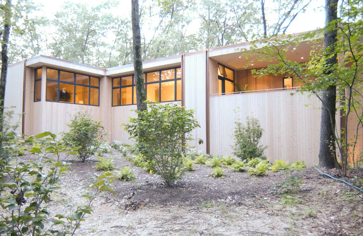 McAllister Road House features vertical wood siding, black window frames, and a covered balcony in a forested site.