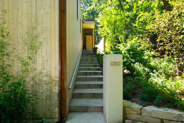 Entry stairway of McAllister Road House with vertical wood siding and lush forest landscaping.