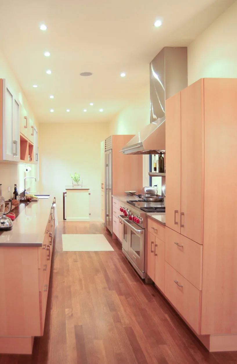 Galley kitchen with warm wood cabinetry and stainless steel range under recessed lighting.