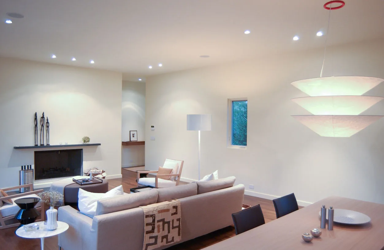 Modern living and dining area with a simple fireplace mantel, wood flooring, and recessed lighting at McAllister Road House.
