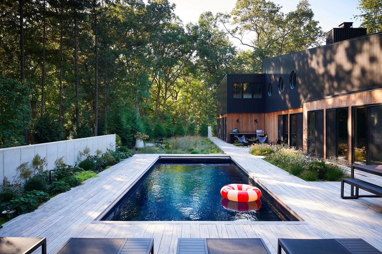 Modern home exterior with a rectangular pool and wood deck surrounded by trees and greenery.