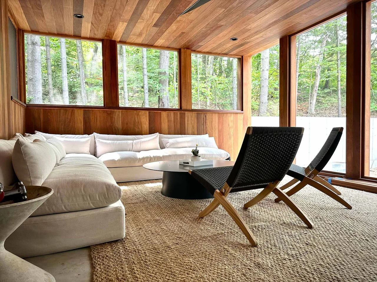 Living space features wood-paneled ceiling and walls with large windows framing the natural landscape outside.