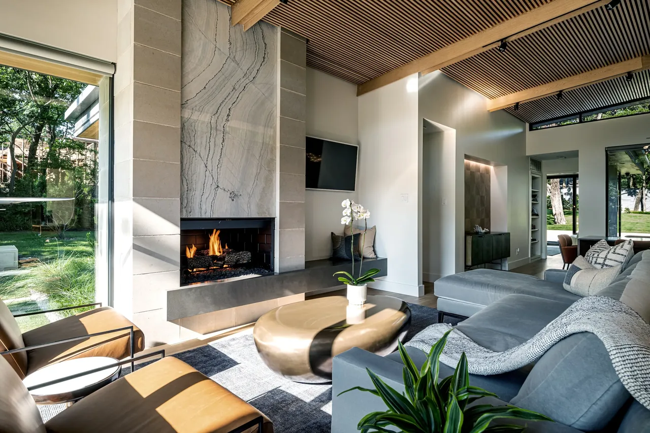 Living room features a wood slat ceiling, stone fireplace, metal framed windows, and abundant natural light.
