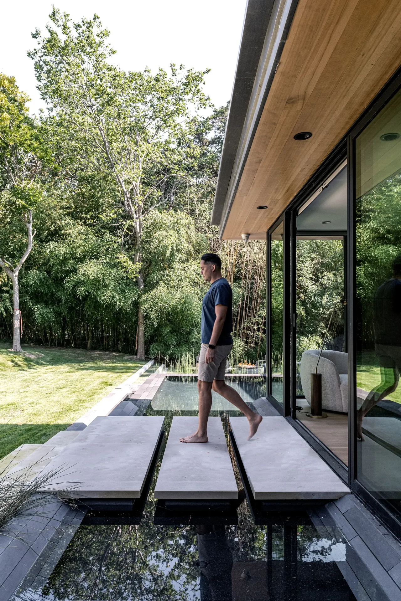 Floating stone slab walkway over a reflecting pool adjacent to a modern home with glass walls.