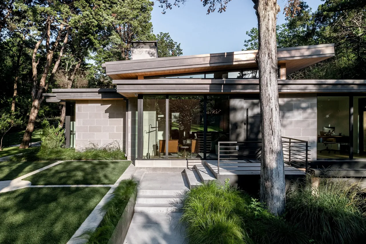 Front exterior of a modern bungalow featuring wood siding, large black window frames, and a stepped concrete entry.