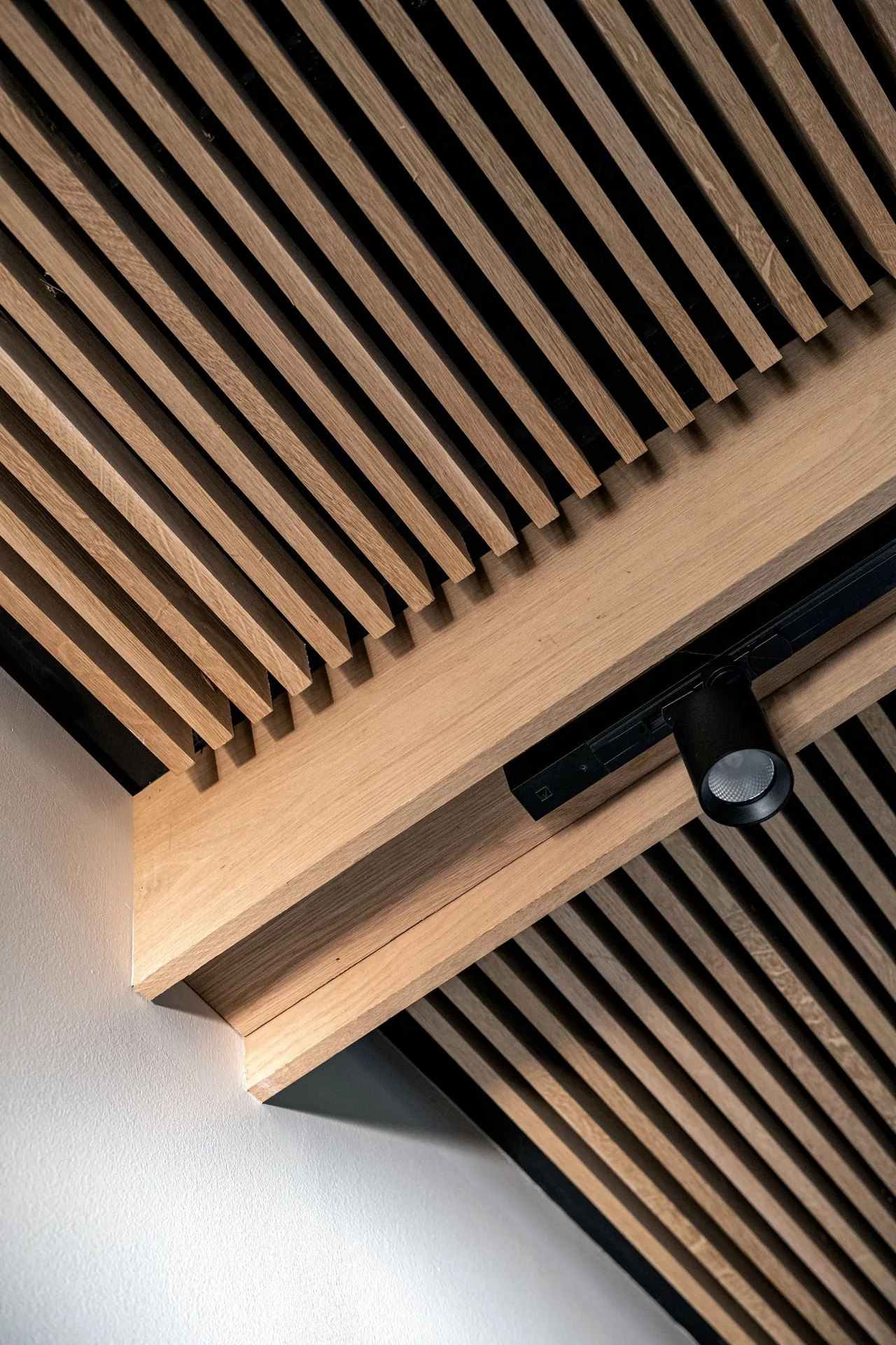 Wooden slat ceiling with a mounted black track light in a modern interior.